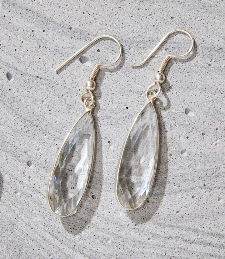 Silver-plated quartz teardrop dangle earrings showcasing clear quartz stones on a textured gray surface