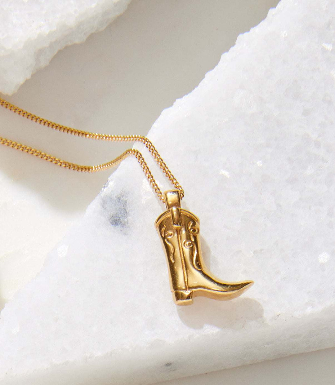Gold cowboy boot necklace pendant on a gold-filled curb chain displayed on white stone surface