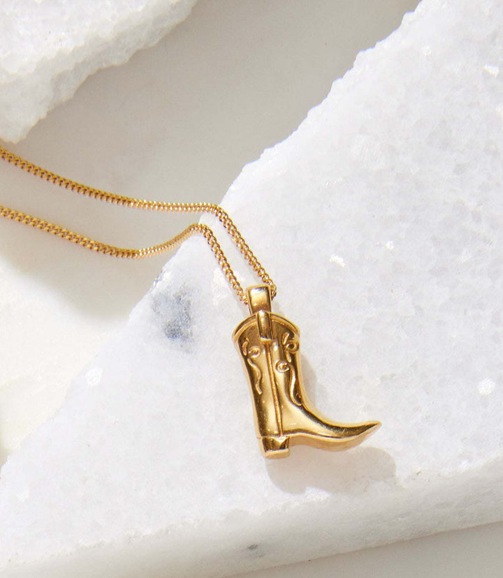 Gold cowboy boot necklace pendant on a gold-filled curb chain displayed on white stone surface