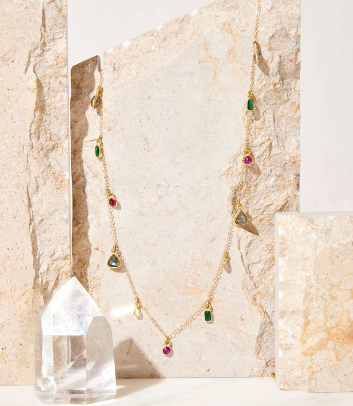 Multicolor gemstone necklace with 14k gold plated chain featuring green, pink, and blue stones on a textured stone background