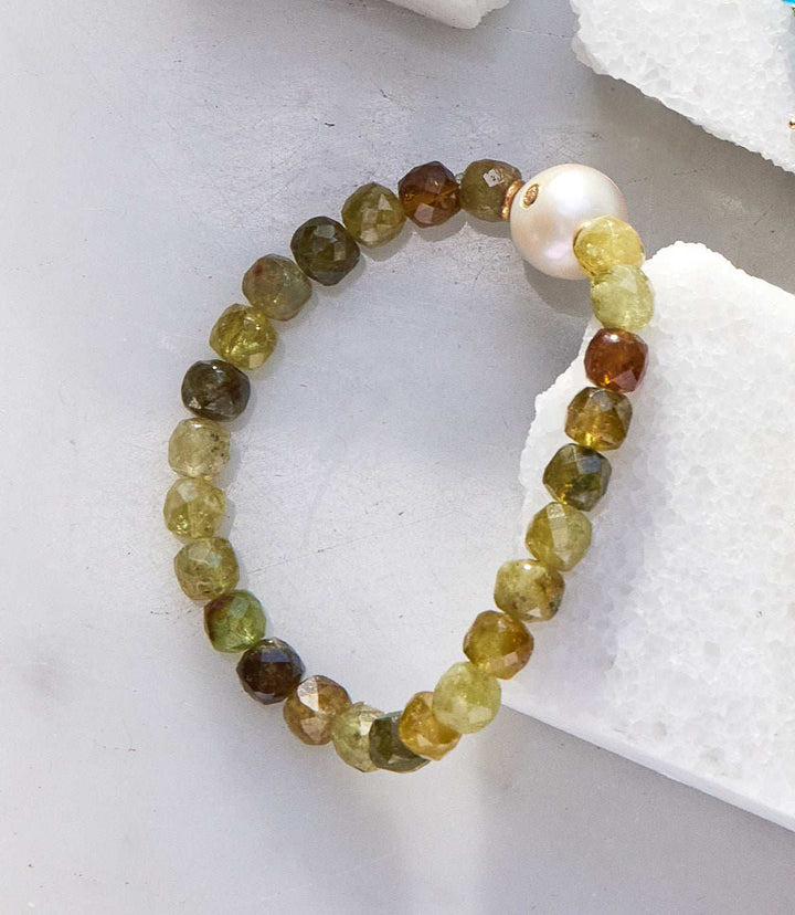 Stretchable gemstone and pearl bracelet featuring multicolored green garnet beads and a single pearl on gold-plated brass.