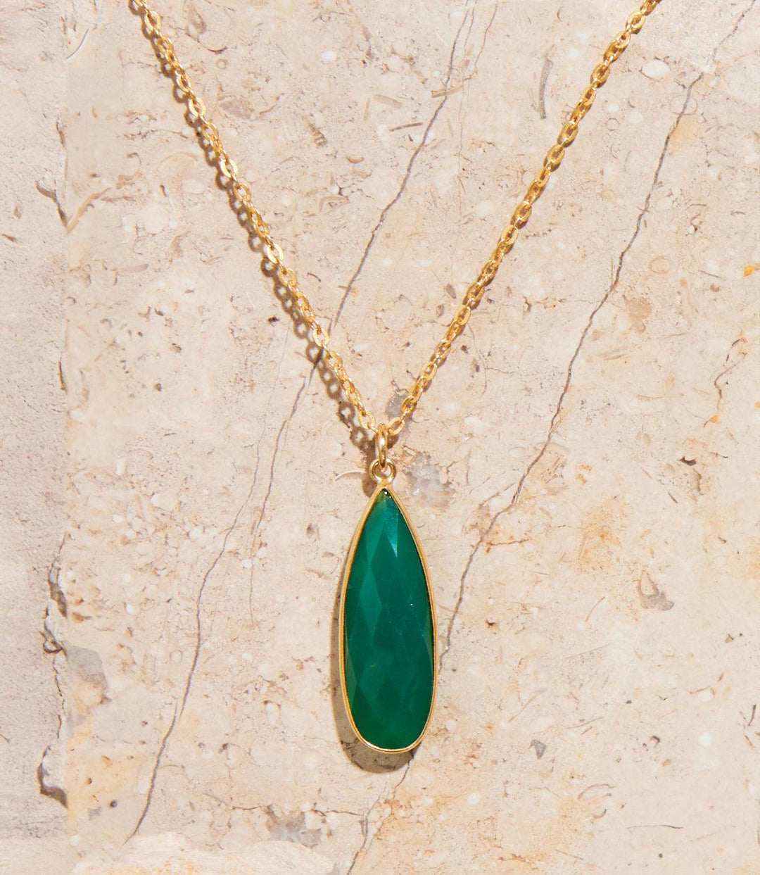 Green onyx quartz necklace with teardrop pendant and gold chain on beige stone background