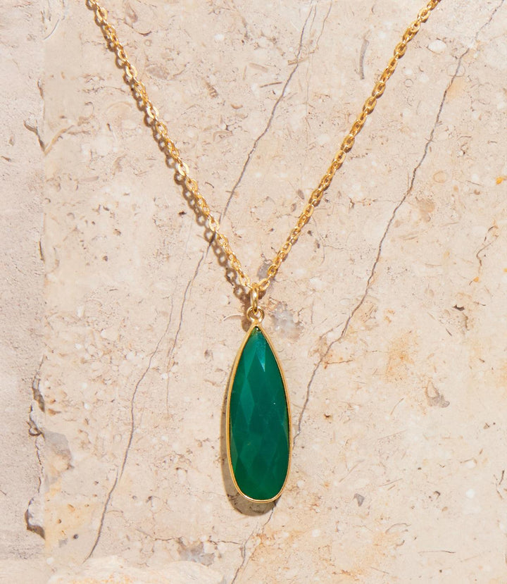 Green onyx quartz necklace with teardrop pendant and gold chain on beige stone background
