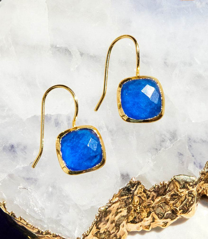 Quartz drop earrings with blue jade cushion cut stones set in 22k gold plated brass hooks on a white crystal background
