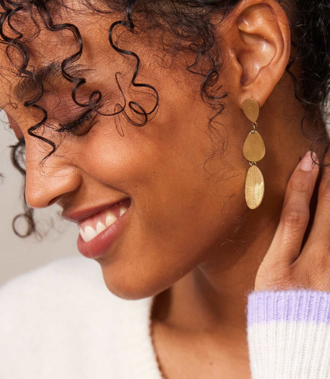 Close-up of a woman wearing handmade gold three drop earrings by Kenyan artisans, featuring organic shapes and a matte finish