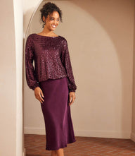 Woman wearing purple satin bias cut midi skirt with sequined long sleeve top in neutral indoor setting