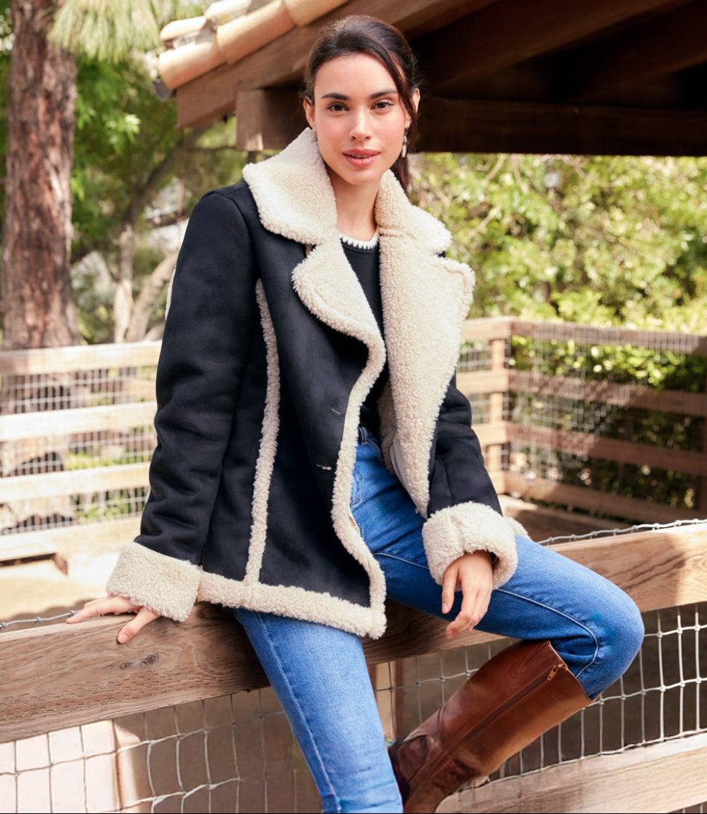 Woman wearing black faux suede shearling jacket with cream trim and blue jeans outdoors