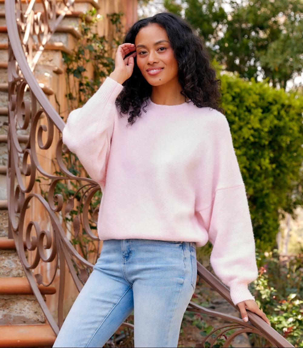 Woman wearing light pink dolman sleeve sweater with crew neck and dropped shoulders outdoors