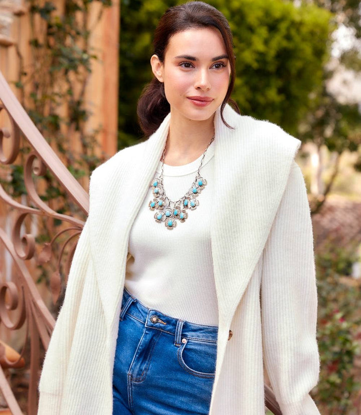 Woman wearing white shawl collar cardigan sweater with raglan sleeves and tortoise shell button closure outdoors