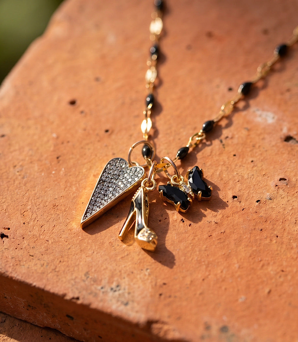 Gold-toned Uptown Girl Charm necklace with pavé heart, high heel, and butterfly charms on black enamel chain