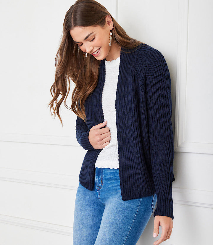 Woman wearing navy blue cropped cardigan sweater with ribbed knit detail over white top and blue jeans