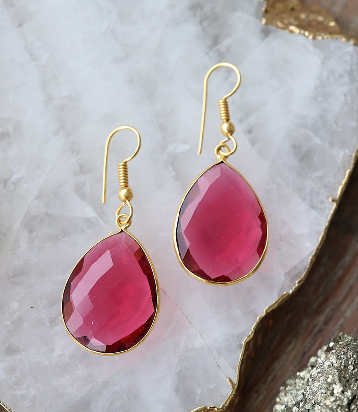Pink quartz teardrop earrings with faceted stones set in gold-filled frames and hook closures on a white quartz surface