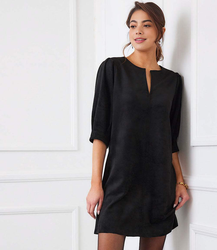 Woman wearing black faux suede puff sleeve dress with split neckline and relaxed straight silhouette
