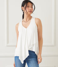 Woman wearing white drape front tank with V-neck and sleeveless design, paired with blue jeans.