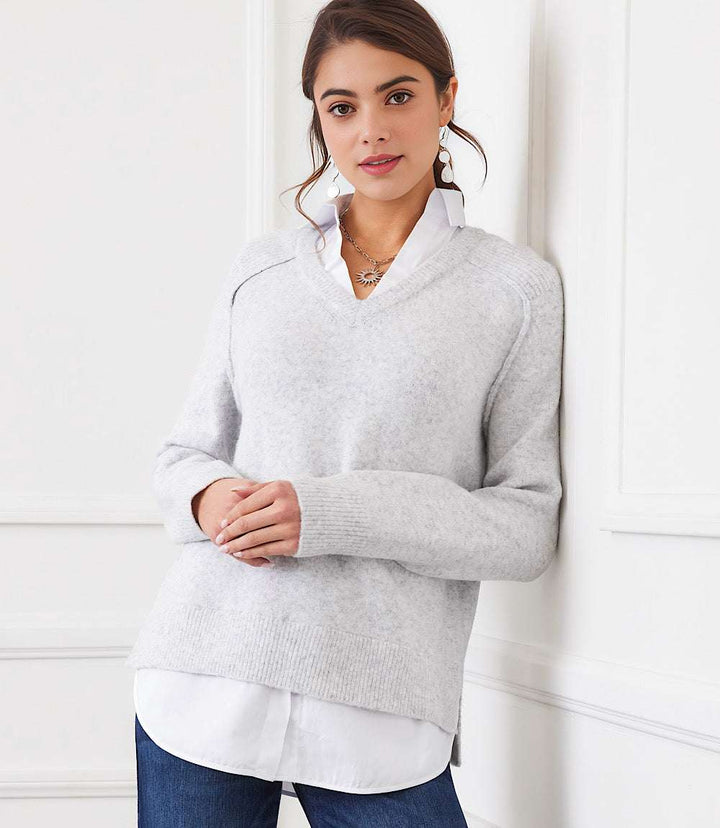 Woman wearing light gray layered sweater with V-neck, collared detail, raglan sleeves, and shirttail hem over white shirt