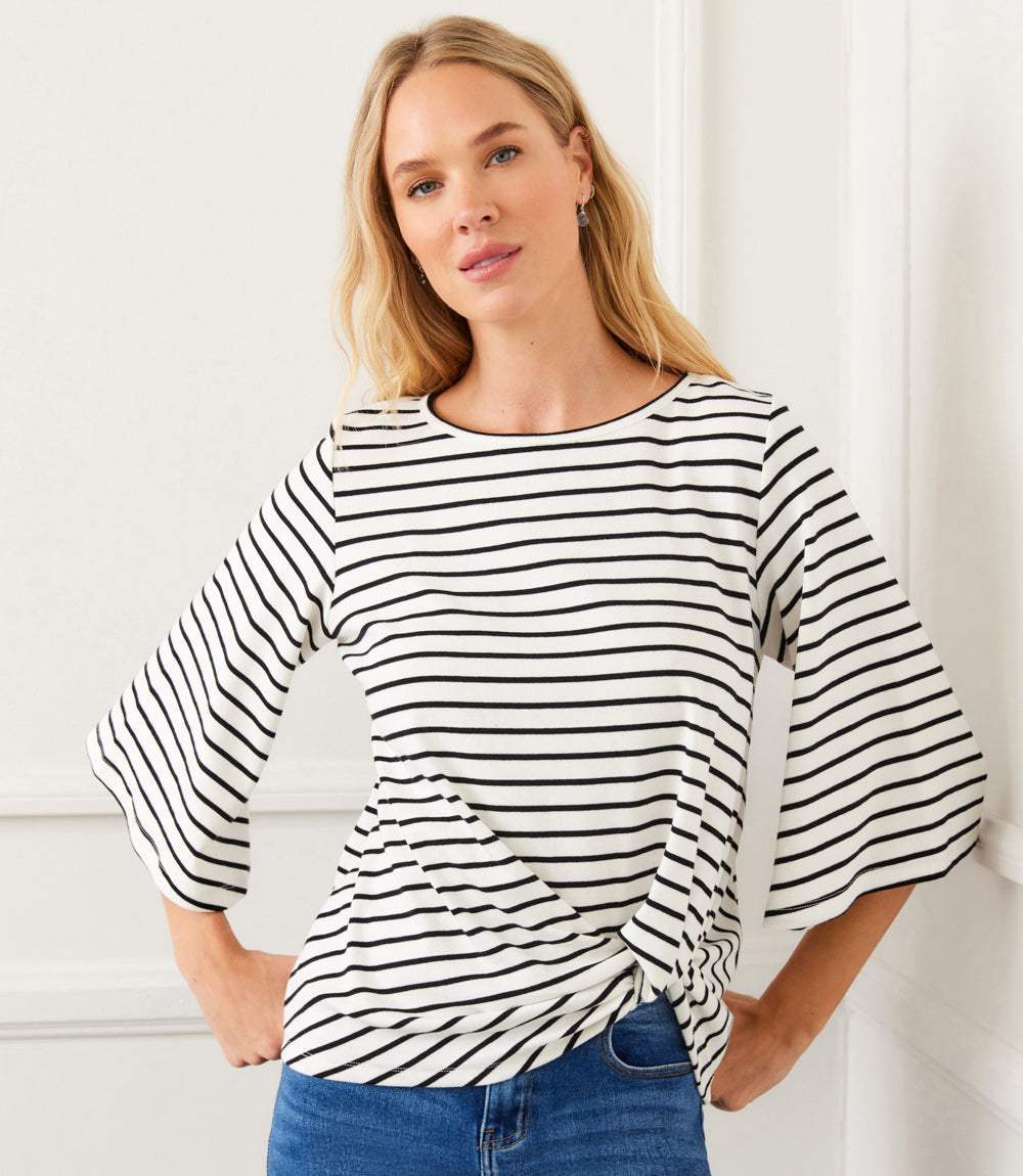 Woman wearing a white and black striped flare sleeve top with front twist hem and scoop neck.