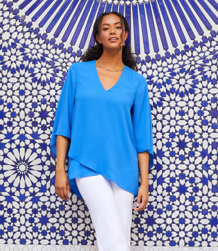 Woman wearing blue Bracelet Sleeve Asymmetric Top with V-neck and layered hem against blue and white tiled background