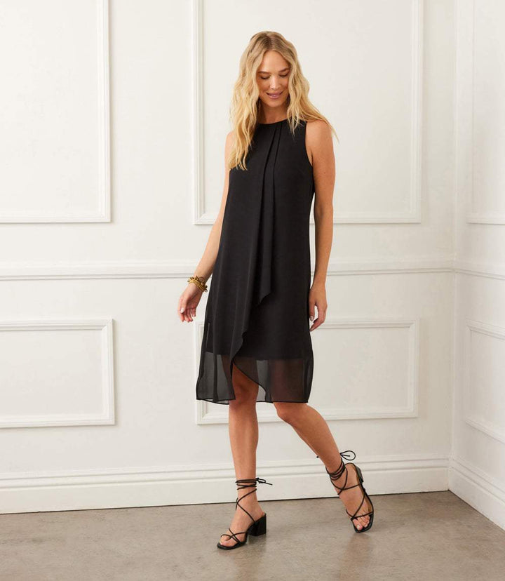 Woman wearing a black sleeveless draped crossover dress with a relaxed fit and chiffon fabric in an elegant room setting