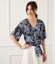 Woman wearing navy blue paisley flutter sleeve tie front top with V-neck and fitted waist