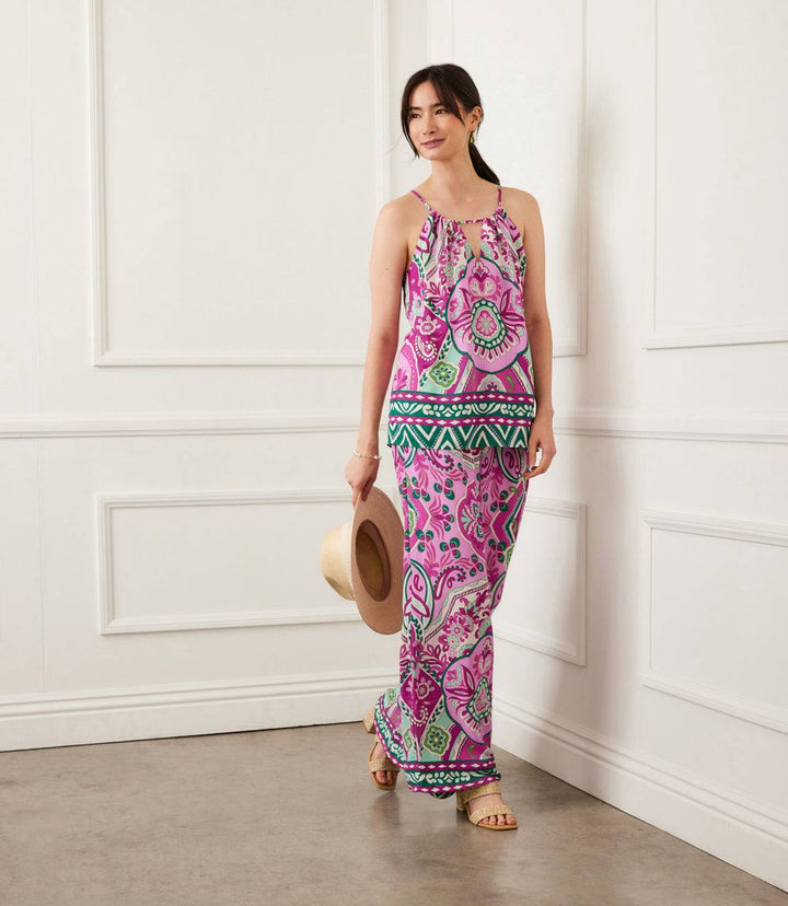 Woman wearing a pink orchid keyhole tank with green and white print, paired with matching skirt, holding a hat indoors