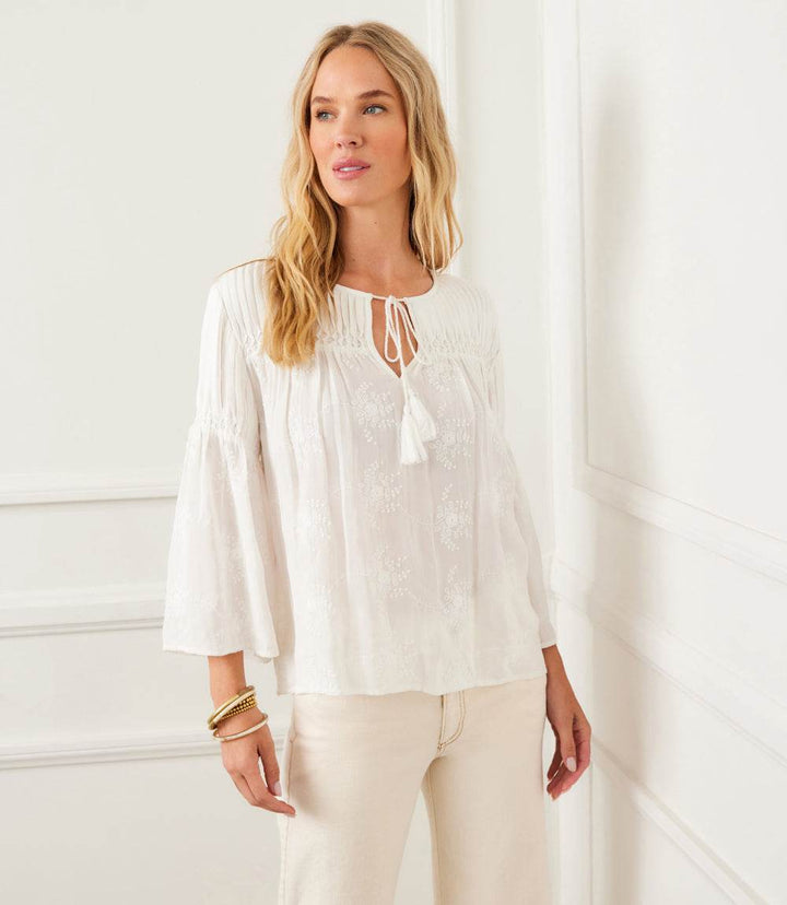Woman wearing white flare sleeve embroidered pintuck detail top with tie neck tassels and relaxed fit