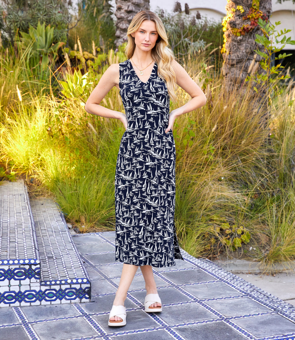 Sleeveless V-neck midi dress with navy background and cream sailboat print, featuring side slit and body-hugging silhouette.
