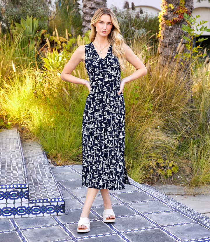 Sleeveless V-neck midi dress with navy background and cream sailboat print, featuring side slit and body-hugging silhouette.