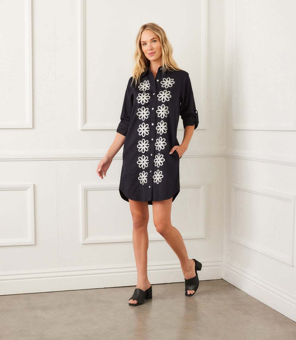 Woman wearing black Roll Tab Embroidered Shirtdress with white floral embroidery, roll-tab sleeves, and side pockets.