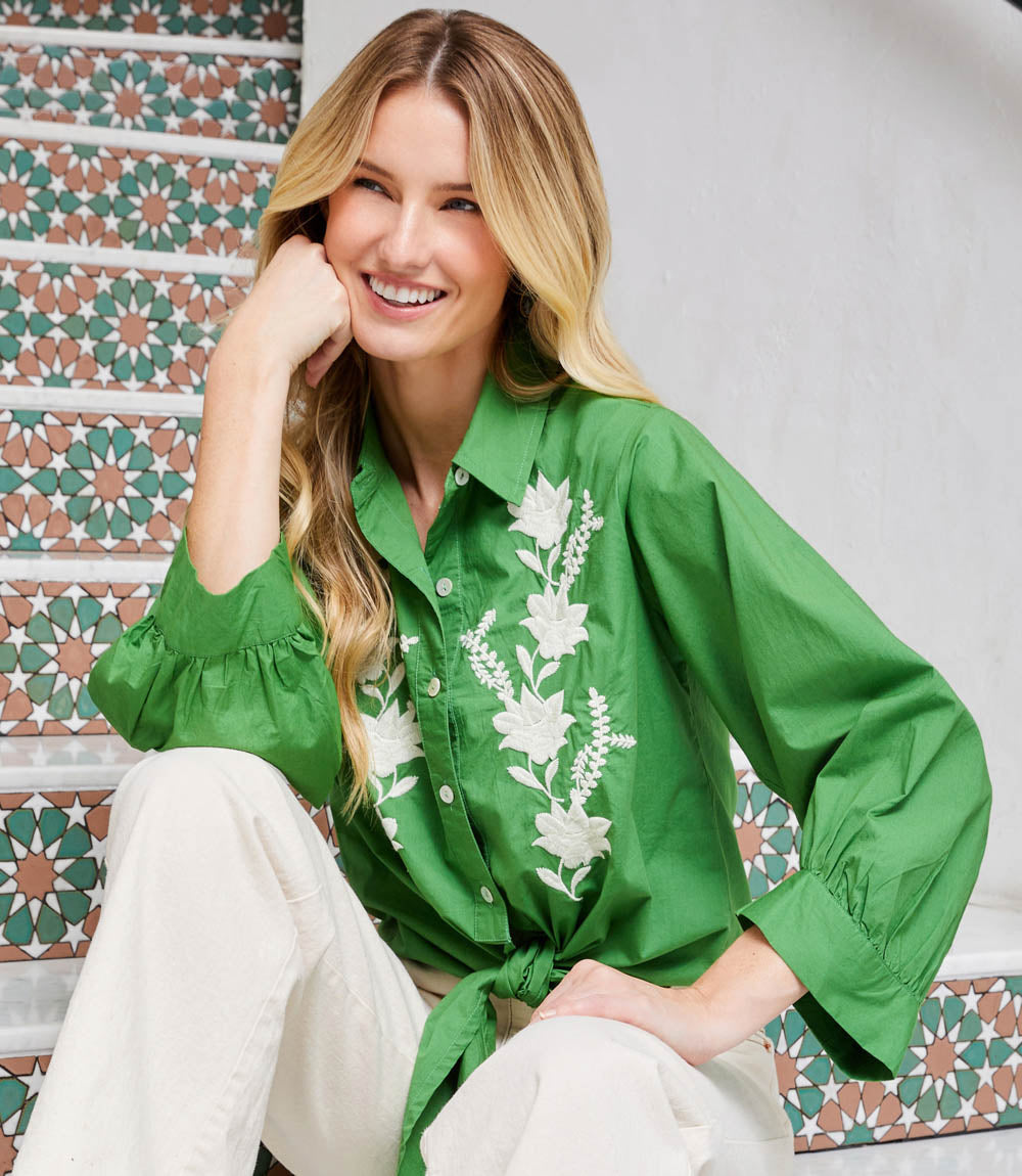Woman wearing green blouson sleeve embroidered tie-front top with white floral details sitting on tiled stairs