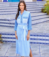 Woman wearing blue and white mixed stripe midi shirtdress with mandarin collar, front buttons, waist tie, and side slits on tiled steps