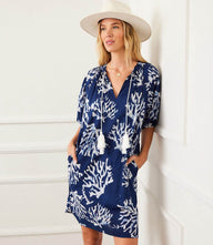 Woman wearing navy blue puff sleeve tassel dress with white coral reef print and tassels, styled with a beige hat