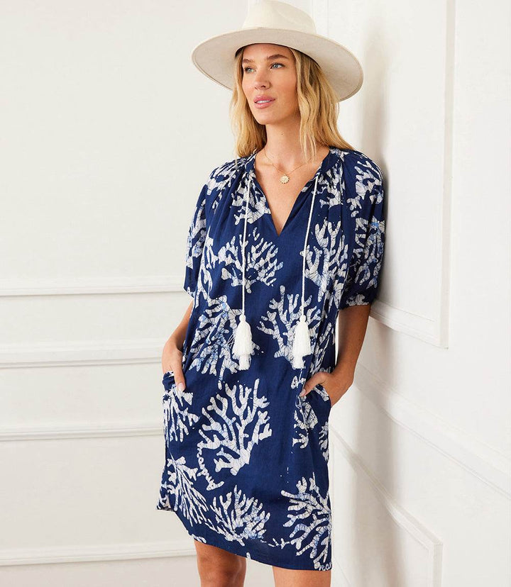 Woman wearing navy blue puff sleeve tassel dress with white coral reef print and tassels, styled with a beige hat