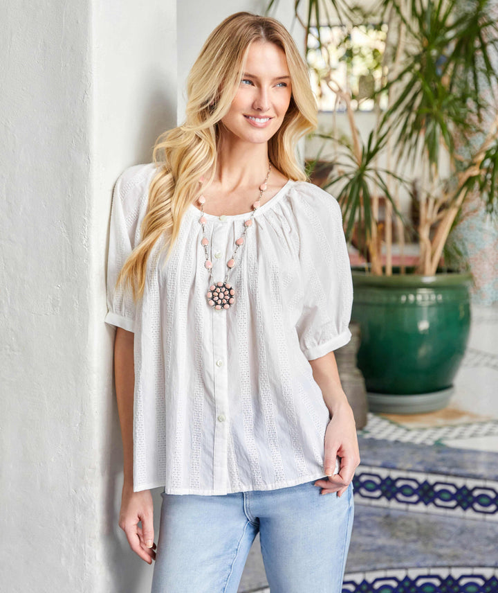Woman wearing a white short sleeve embroidered peasant top with button-up front and puff sleeves.