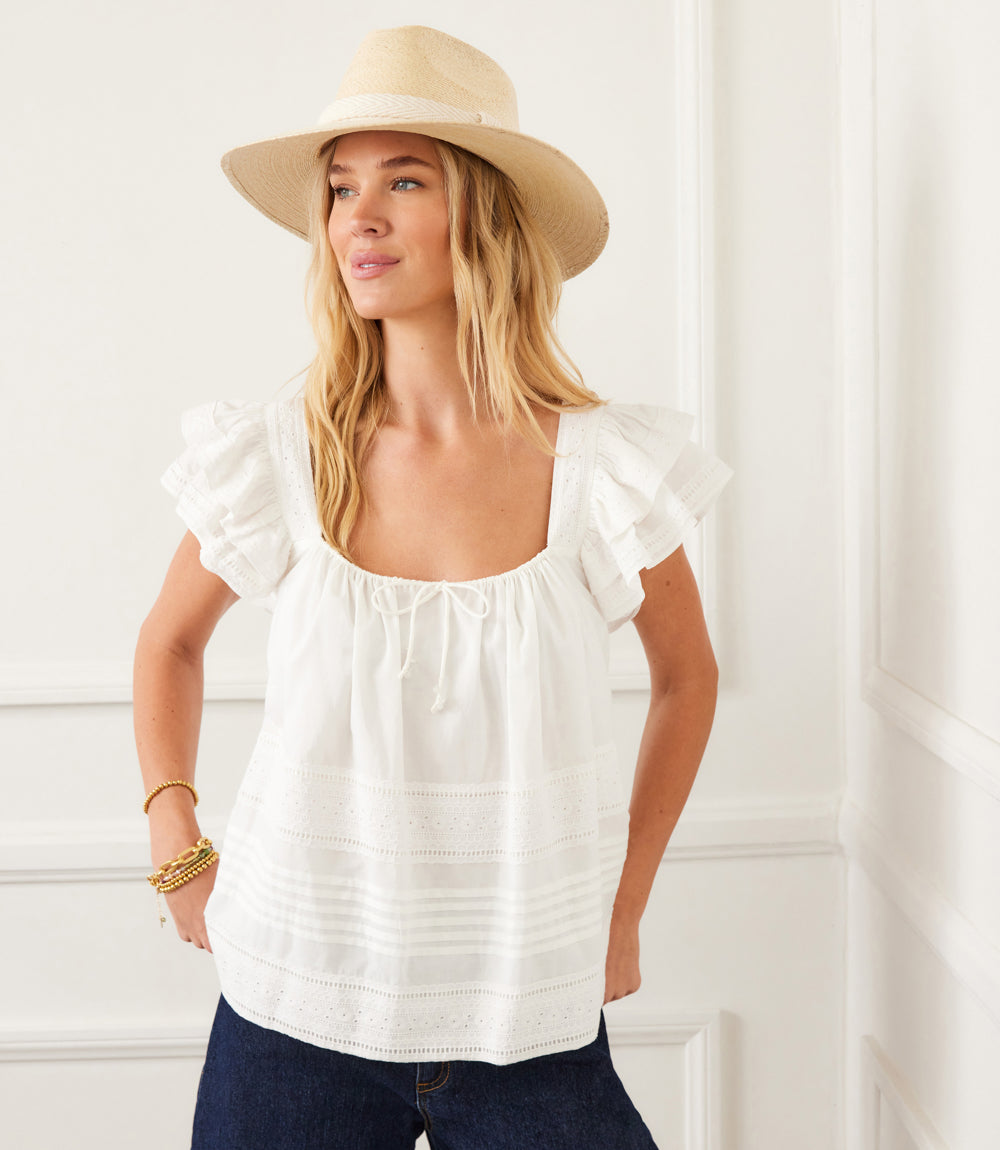 Woman wearing white embroidered ruffle sleeve blouse with square neck and casual hat