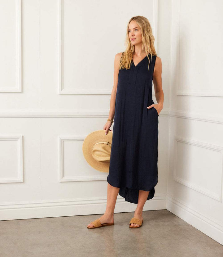 Sleeveless navy midi dress with V-neckline, front placket, side pockets, and shirt-tail hem, perfect for warm weather.