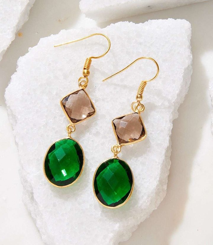 Gold plated multi gemstone earrings with green emerald and topaz glass stones on white textured background