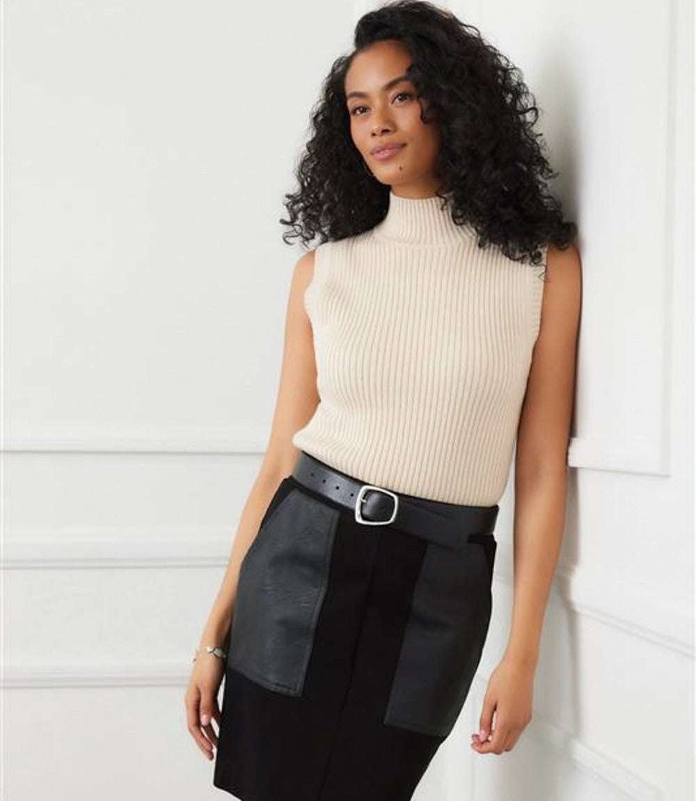 Woman wearing a beige ribbed turtleneck sleeveless sweater tank paired with a black skirt and belt.