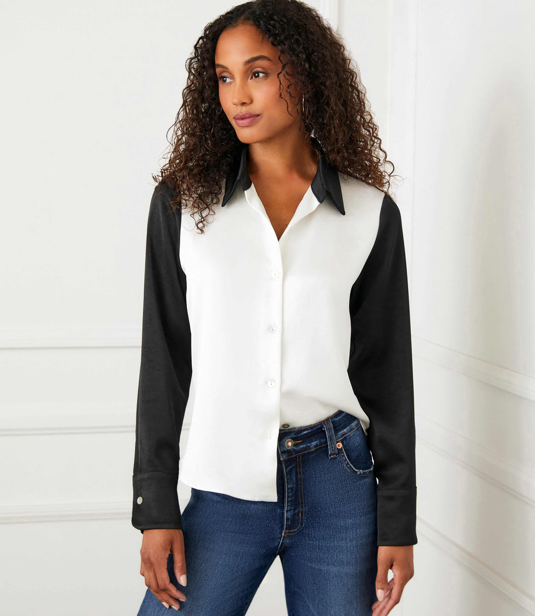 Woman wearing long sleeve satin colorblock shirt with black sleeves and collar and white body paired with blue jeans