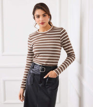 Woman wearing brown and white stripe long sleeve crewneck top with black leather skirt inside white room