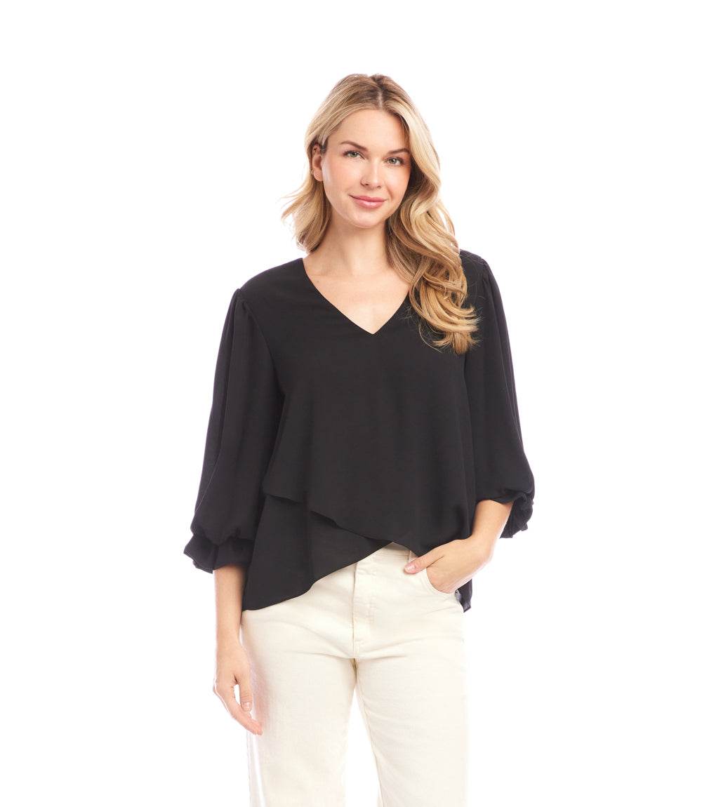 Woman wearing black layered sleeve asymmetric top with V-neck and bishop sleeves paired with light-colored pants
