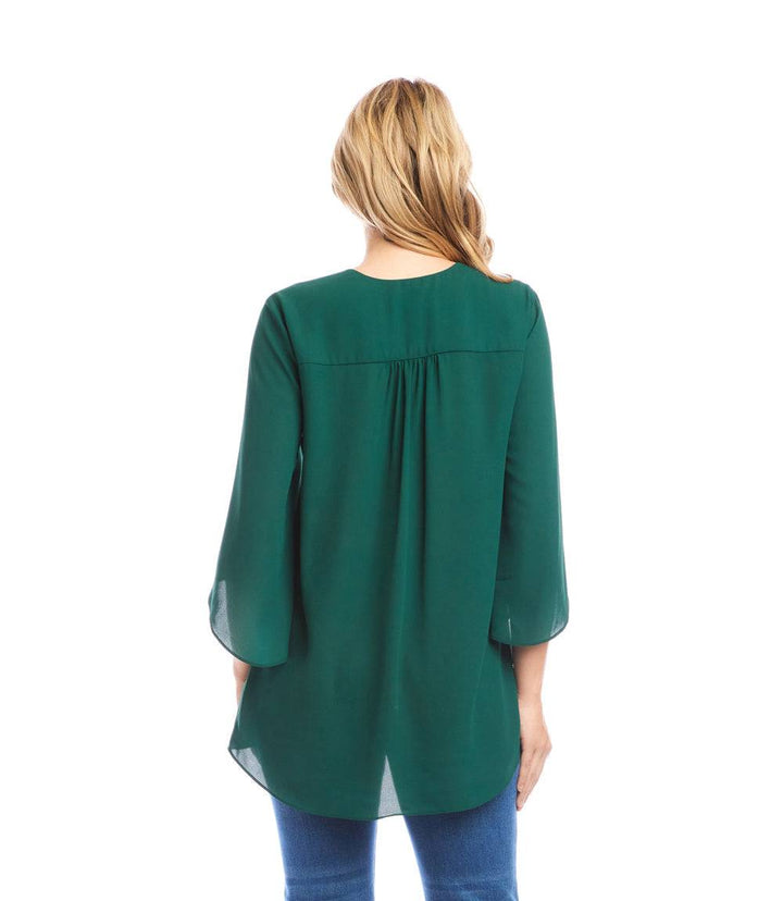 Woman wearing a green petite size asymmetric top with bracelet sleeves and layered hem, shown from the back