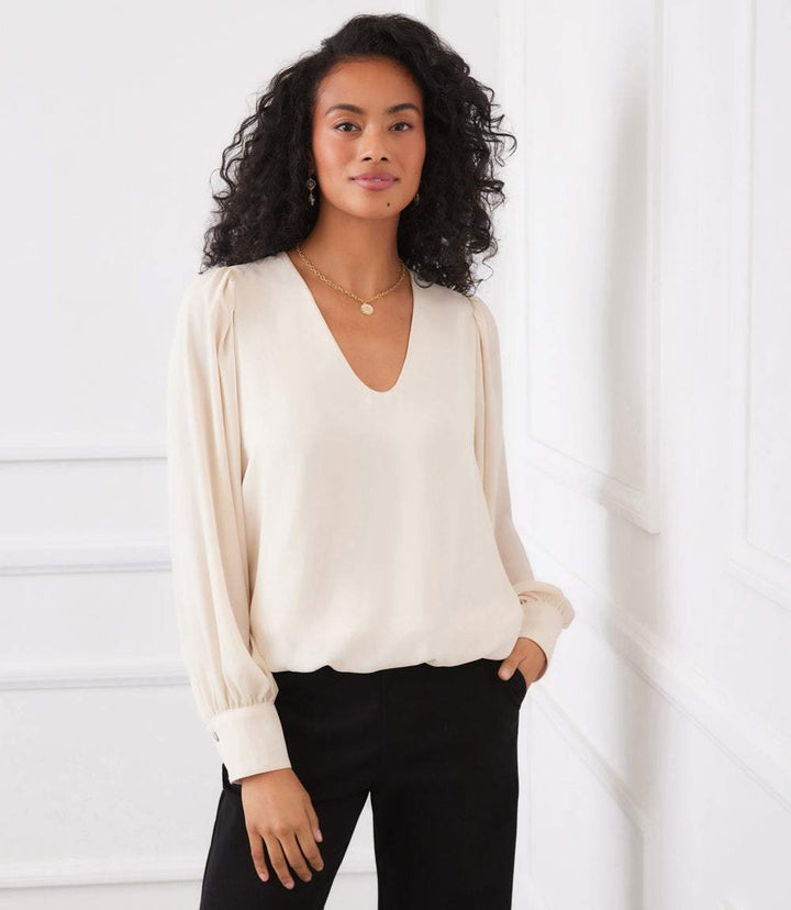 Woman wearing elegant cream puff sleeve V-neck top with long sleeves and buttoned cuffs