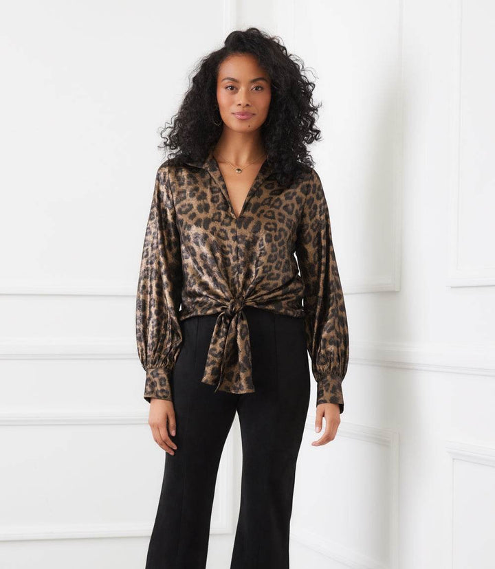 Woman wearing shimmer leopard print long sleeve tie-front top with collared neckline and buttoned cuffs paired with black pants