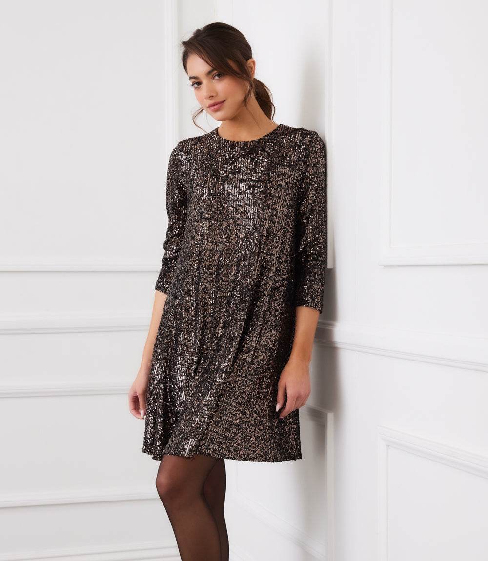 Woman wearing a 3/4 sleeve sequin swing dress with scoop neckline and back keyhole closure, above knee length.