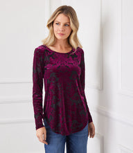 Woman wearing a long sleeve velvet burnout top in wine and black with scoop neck and shirttail hem