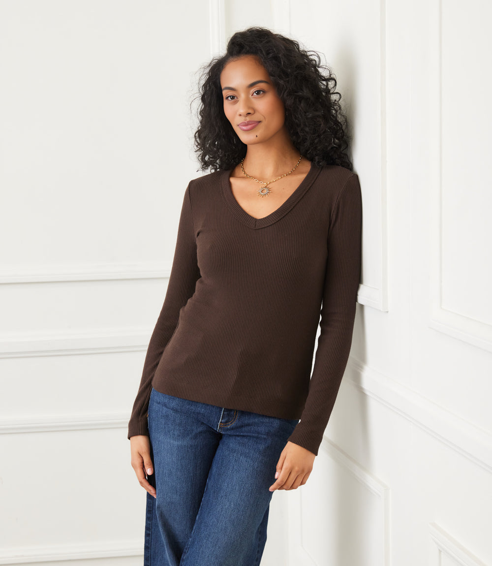 Woman wearing a fitted long sleeve ribbed V-neck top in brown paired with blue jeans indoors