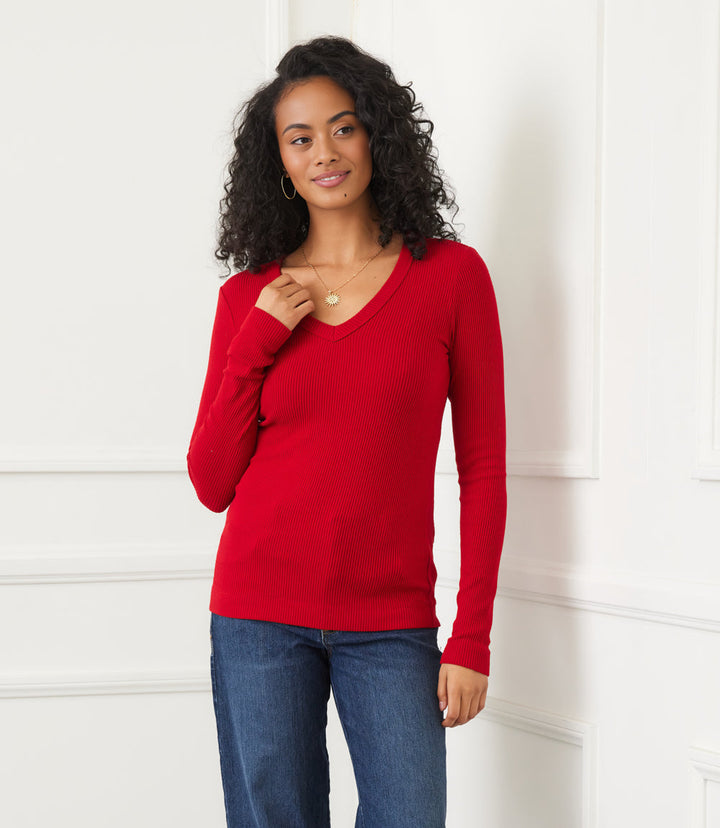 Woman wearing red long sleeve ribbed V-neck top with jeans standing indoors