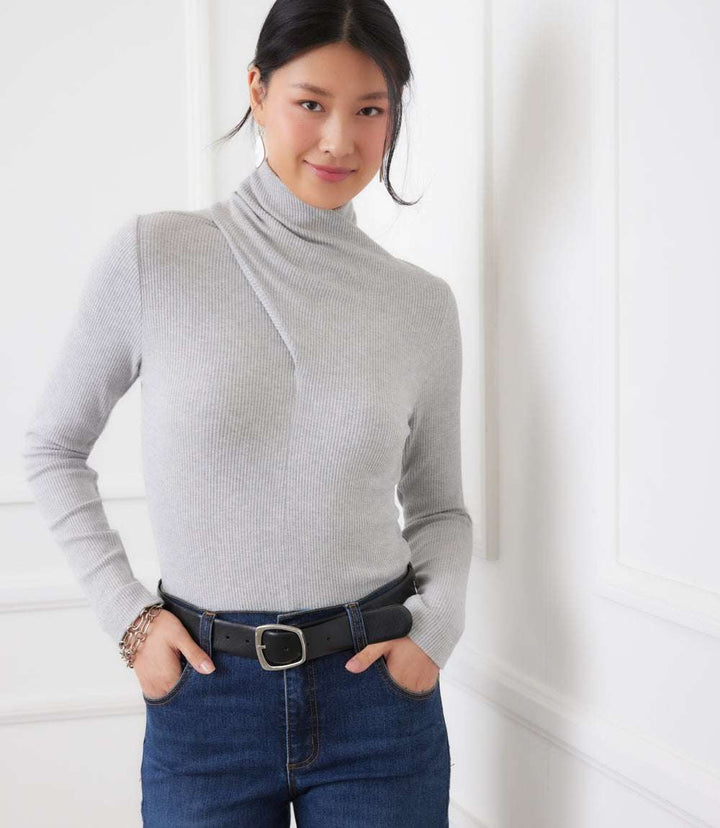 woman wearing gray ribbed faux wrap turtleneck top with long sleeves and slim fit tucked into blue jeans