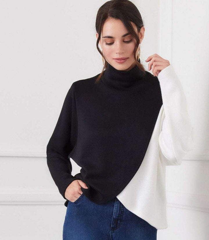 Woman wearing long sleeve crossover colorblock top with mock neck and curved hemline in black and white