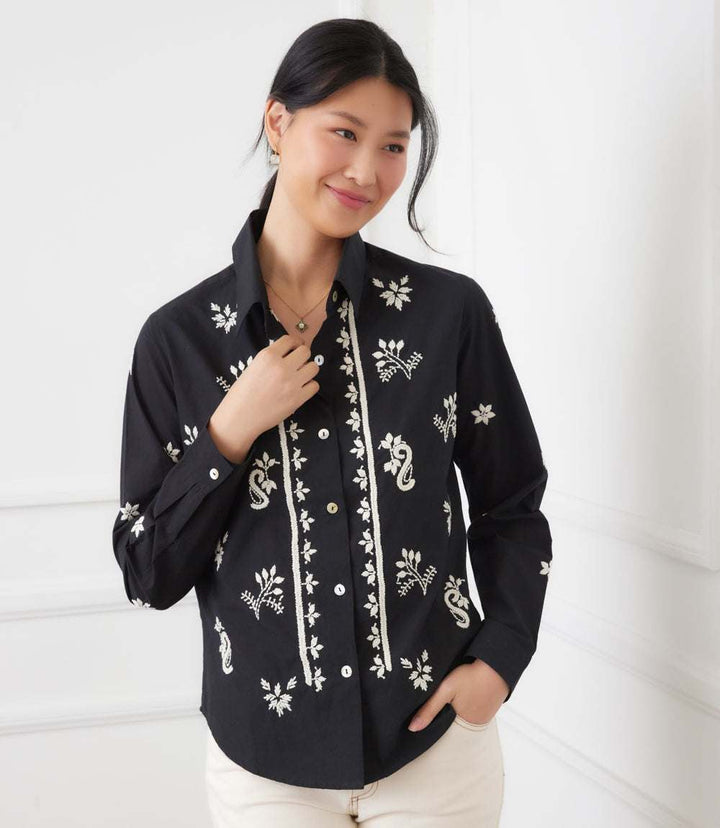 Black long sleeve embroidered shirt with cream floral and paisley embroidery, button front, and collared neckline worn by smiling woman